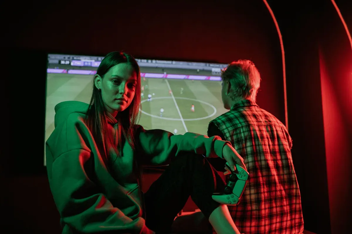 Two gamers under green and red light with a football game on screen