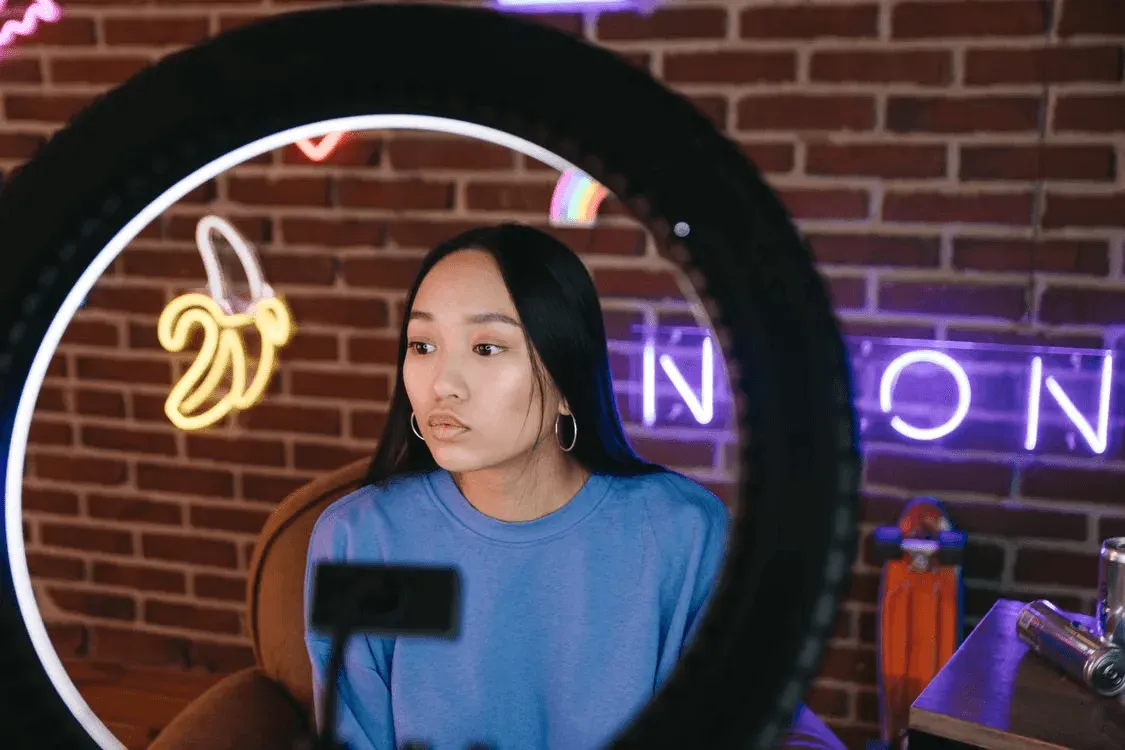 Creator filming through a ring light against a brick wall with neon signs
